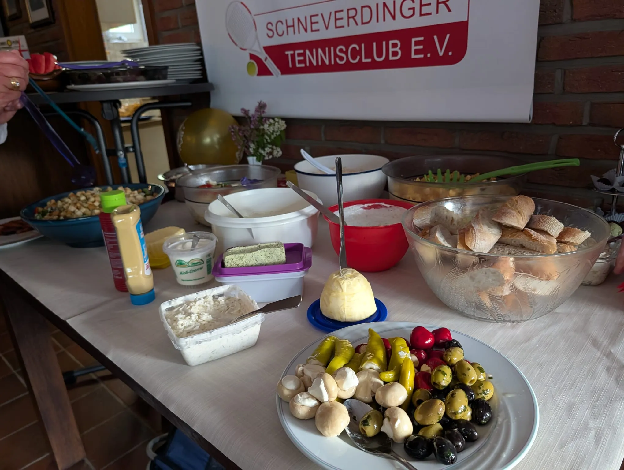 Buffettisch mit Salaten, Dips, Brot und einem Teller Oliven und Antipasti vor dem Banner des Schneverdinger Tennisclub e.V.