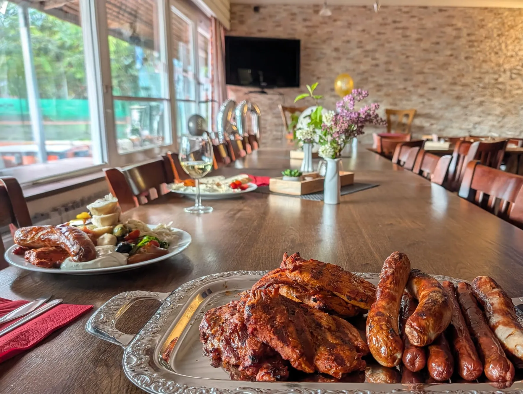 Silberne Platte mit gegrilltem Fleisch und Würstchen auf einem langen Tisch im Vereinsheim, dahinter Blumen und Luftballons.